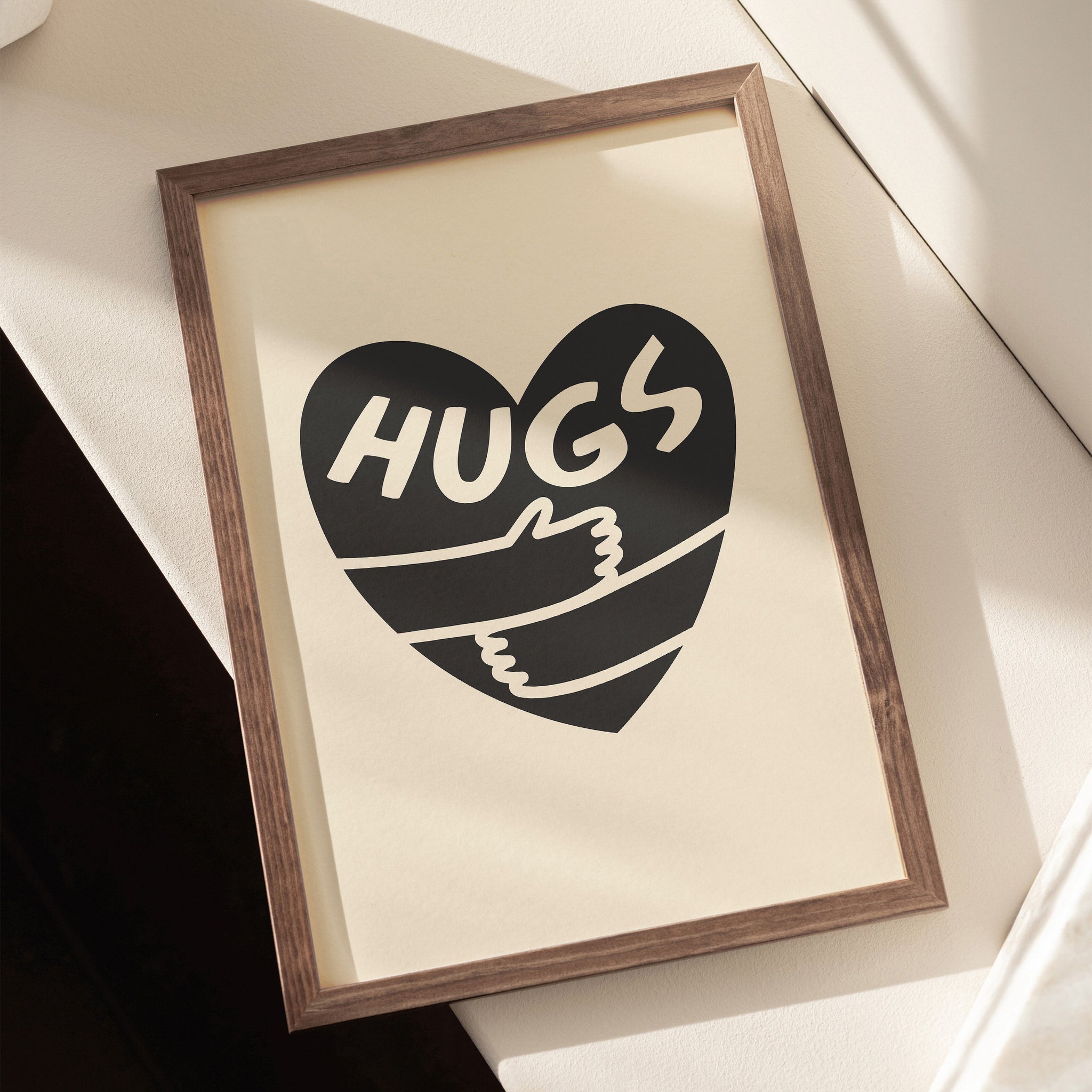 Black heart poster with arms embracing and 'Hugs' text on a neutral beige canvas